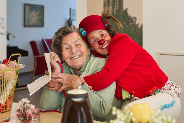 Eine Clownin umarmt eine lachende Bewohnerin